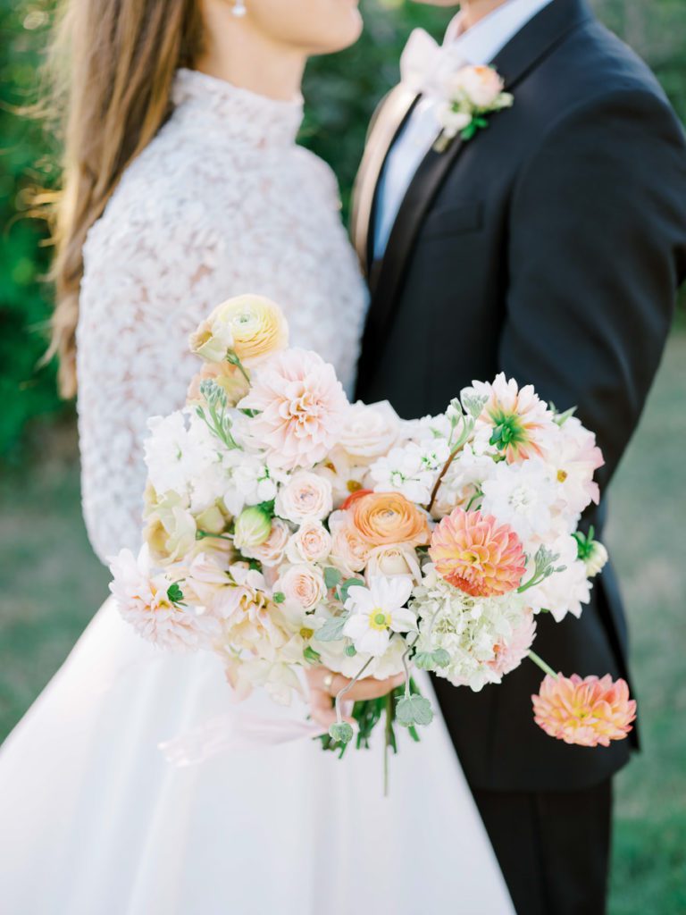 Wedding bouquet of light pinks, coral and yellow featuring dahlias, and rananculus blooms 