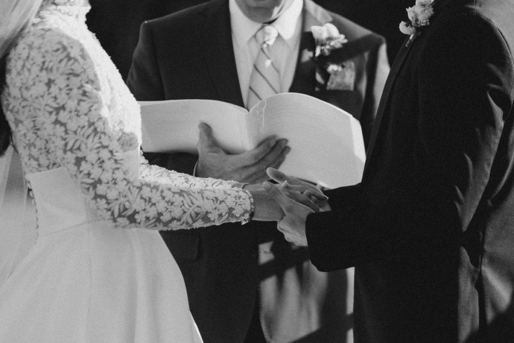 bride and groom holding hands during wedding ceremony in black and white