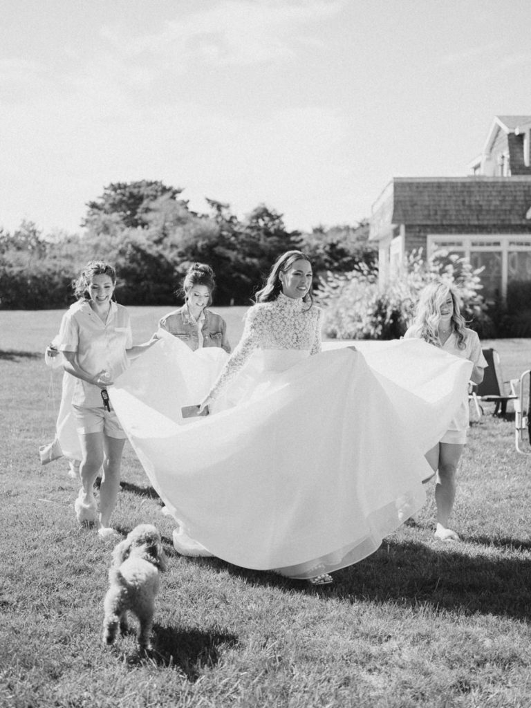 bride walking to first look with her bridesmaids helping her with her dress and puppy following along 