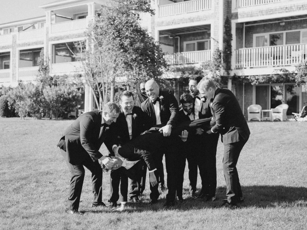 groomsmen laughing as they almost drop the groom after picking him up for photo