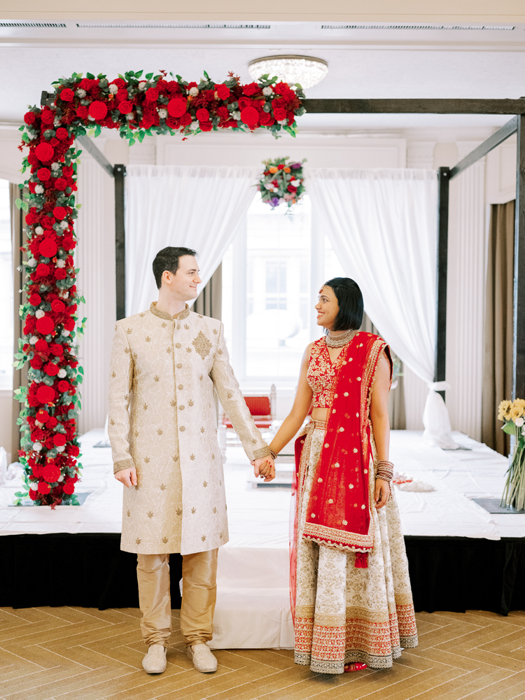 Indian Wedding Bride and Groom at Hindu Ceremony with Red Florals in a Red and Tan Saree and Tan sherwani