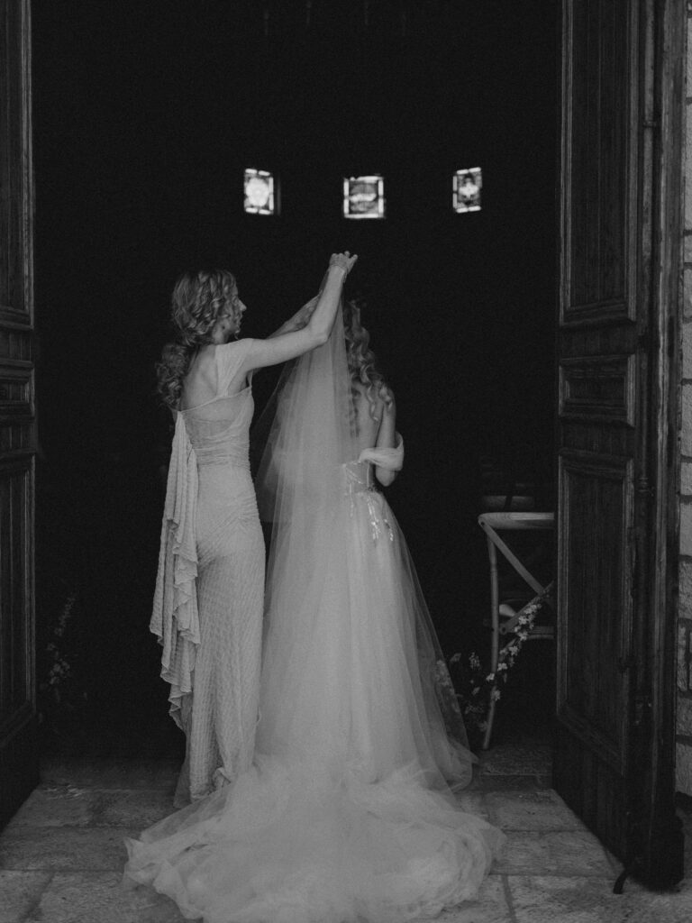 Bride's sister helping her adjust veil before heading down the aisle to ceremony | black and white